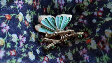 Gerry's broche goudkleurige vlinder op tak met groene strass en twee kleuren groen emaille op vleugels op bloemetjesstof