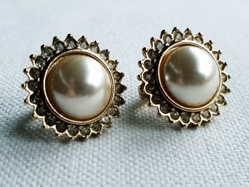 Oorbellen met één grote parel omringd door heldere strasssteentjes in goudkleurige setting op doek