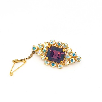 Rhinestone aurora borealis brooch with purple center stone and safety chain