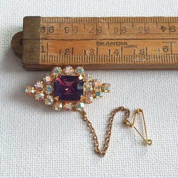 Rhinestone aurora borealis brooch with purple center stone and safety chain