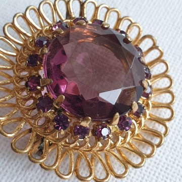 Round goldtone brooch with amethist coloured glass stone closeup