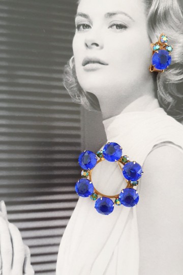 Set van oorbellen en ronde broche met koningsblauwe stenen en heldere strasssteentjes op foto